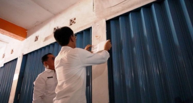 Petugas dari Pemerintah Kabupaten Ogan Komering Ilir sedang melakukan pemasangan stiker pada kios pedagang yang menunggak retribusi di Pasar Rakyat Kayuagung, pada hari Rabu, tanggal 3 Desember 2025. (foto : Humas Pemkab OKI)